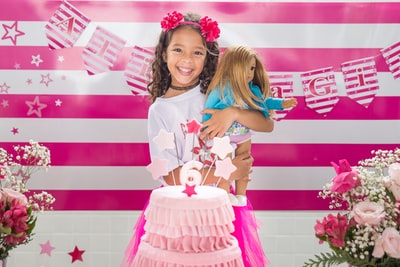 女孩幸福的微笑与粉红娃娃蛋糕在她的面前
